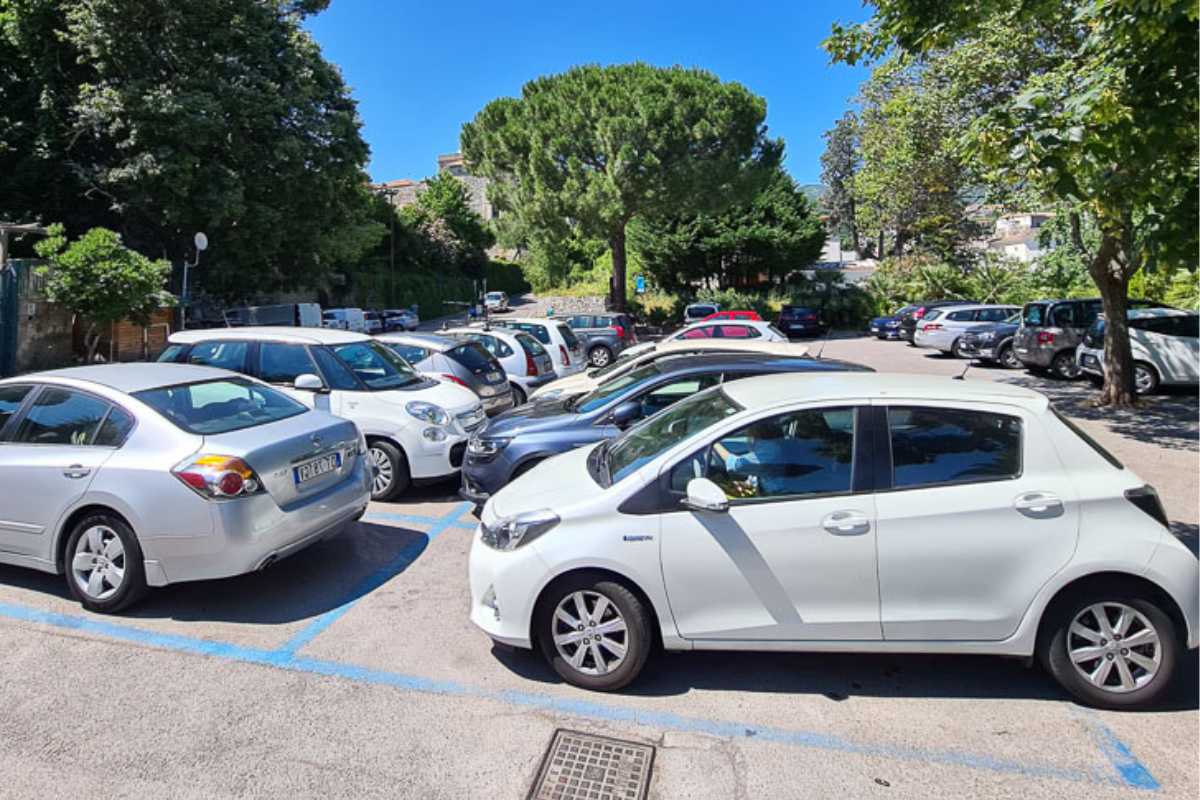 Scorcio panoramico di Ostuni al tramonto, con auto parcheggiate ai piedi delle mura bianche e il centro storico in vista