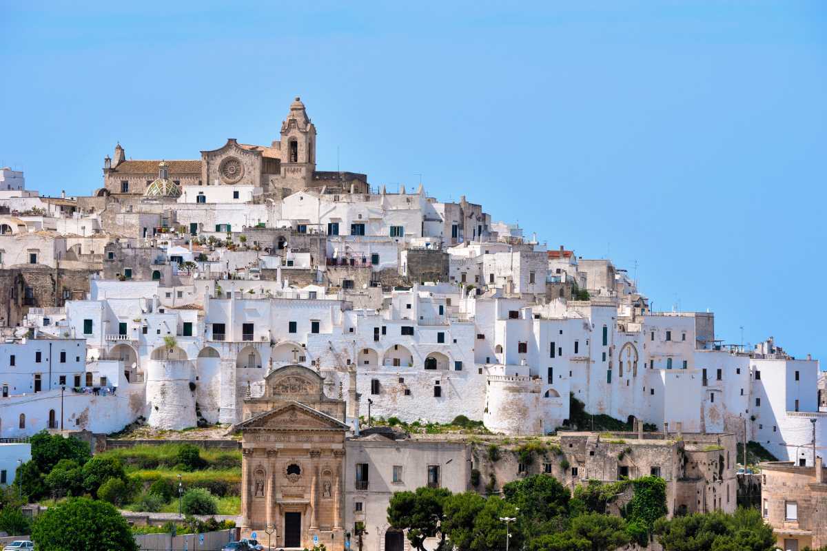 Scorcio panoramico del centro storico di Ostuni decorato a festa, con luminarie e folla in festa. Atmosfera serale, dettagli delle architetture bianche.